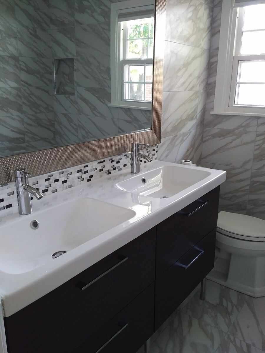 After: bathroom with large-format marble-look tile, a double-sink vanity with dark drawers, and a mosaic backsplash